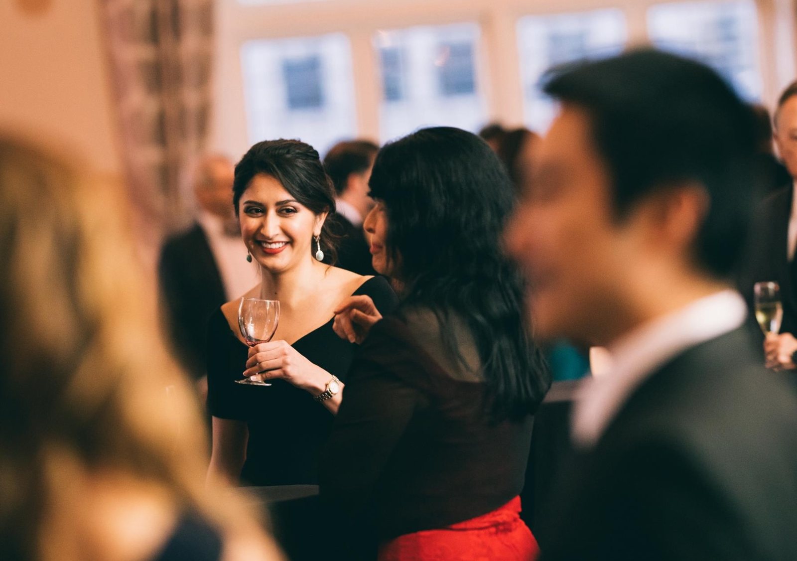 Members in evening wear sharing a laugh over drinks at a Club reception